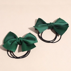 Détail de deux chouchous à nœud en satin vert foncé avec des bandes élastiques