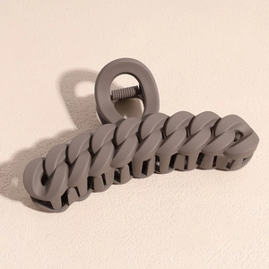 Macro detail of matte dark brown hair claw clip with chain link design on light beige background