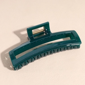 Detail of dark green square hair claw clip with golden spring on textured background