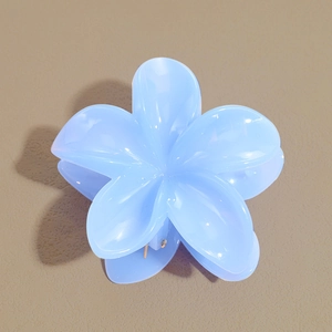 Gros plan sur la pince à cheveux en forme de fleur de frangipanier bleu clair et brillante