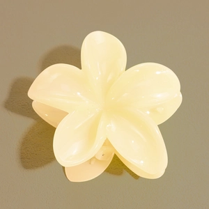 Vue de dessus d'une pince à cheveux en forme de fleur de frangipanier crème sur fond vert