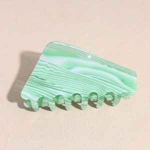 Macro shot of green and white marble pattern acetate hair claw clip on beige backdrop
