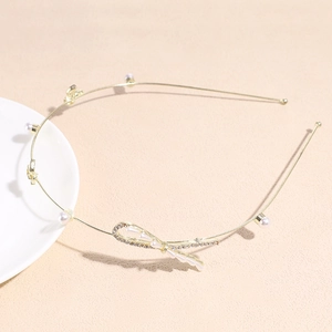 Détail d'un serre-tête doré fin orné d'un papillon en cristal et perles blanches