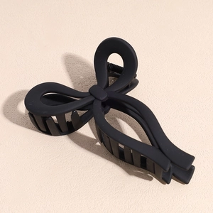 Close-up of a matte black bow hair claw clip for women on a beige textured surface