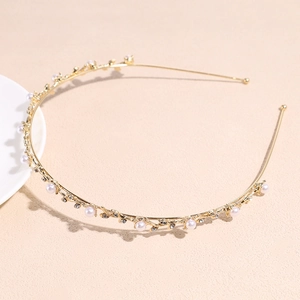 Détail du serre-tête doré orné de perles blanches et strass brillants sur fond texturé