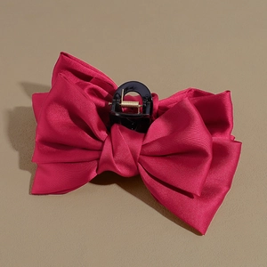 Close-up of a large red satin bow hair claw clip showing smooth fabric and metal spring