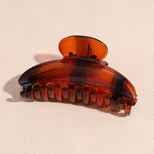 Macro detail of amber acrylic hair claw clip showing polished teeth and metal spring