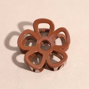 Detail of a brown flower-shaped hair claw clip with glossy finish and metal spring