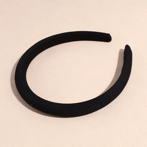 Dettaglio di un cerchietto imbottito in tessuto nero opaco su una superficie beige