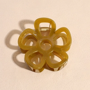 Translucent amber flower hair claw clip with golden metal spring on a textured background