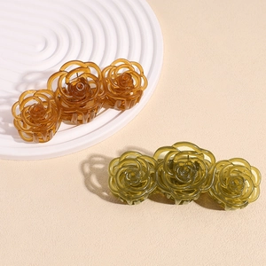 Elegant rose floral hair claw clips in amber brown and olive green on a white pedestal