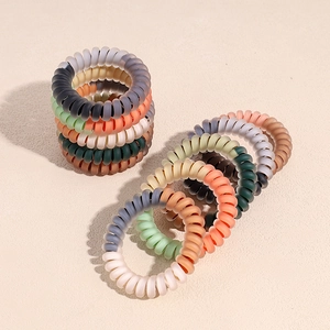 Élastiques à cheveux spirale mats de couleurs Morandi empilés sur une surface beige
