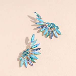 Exaggerated wing-shaped earrings with blue crystals and gold finish on cream background