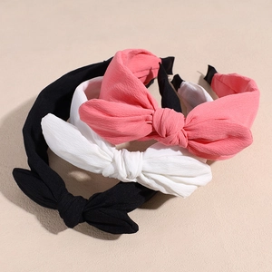 Set of three chiffon bow headbands in black, white, and coral pink on beige surface