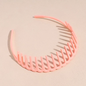 Détail d'un serre-tête ondulé rose mat avec dents antidérapantes sur fond beige texturé