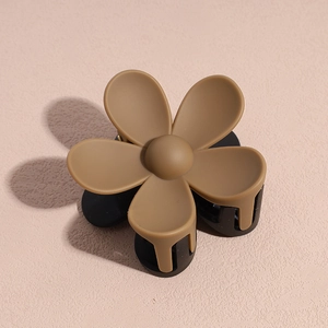 Détail de la pince à cheveux fleur mate marron et noire sur fond clair texturé