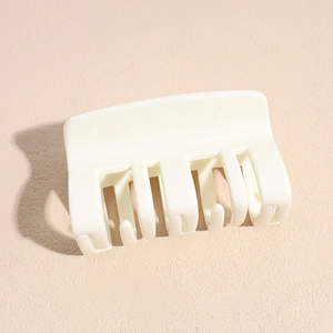 Détail d'une pince à cheveux carrée crème mate avec plusieurs dents sur fond rose