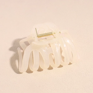 Détail d'une grande pince à cheveux blanc crème avec ressort doré et design ondulé