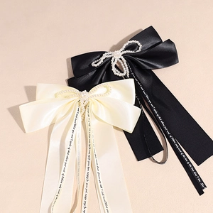 Detail of satin bow hair clips with pearl centers and elegant script ribbons
