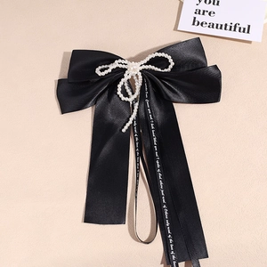 Detail of a large black satin bow hair clip with faux pearl trim and elegant white ribbons