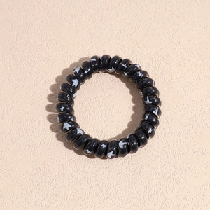 Detail of a thick black spiral hair coil with white star patterns on a beige surface