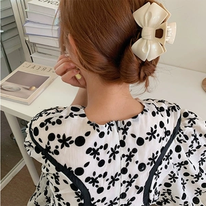 Elegant cream-colored acrylic bow hair claw clip for bun styling on a woman back view