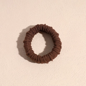 Dettaglio dell'elastico per capelli in tessuto a coste marrone su sfondo beige
