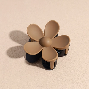 Détail d'une pince à cheveux fleur mate marron caramel et noir sur surface texturée