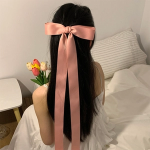 Detailed view of large pink satin bow hair clip with long ribbons on long black hair