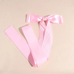 Macro detail of glossy pink satin ribbon bow hair clip with long flowing streamers