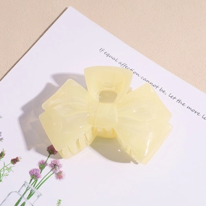 Close-up of a pale yellow acrylic bow hair claw clip with a glossy resin finish