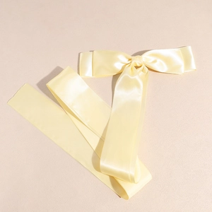 Detailed view of long pale yellow satin ribbon hair bow with glossy silk texture finish