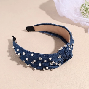 Detail of blue denim knot headband with pearls and rhinestones on beige background