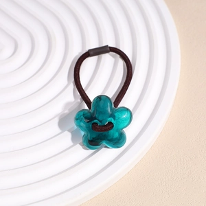 Détail macro d'un élastique à cheveux fleur en résine cyan sur un plateau blanc