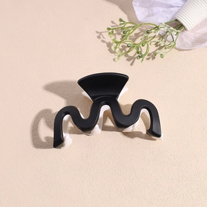 Détail de la pince à cheveux ondulée mate en noir contrasté et blanc crème