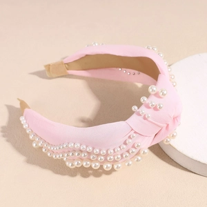 Détail du serre-tête rose noué avec perles blanches sur une texture de tissu doux