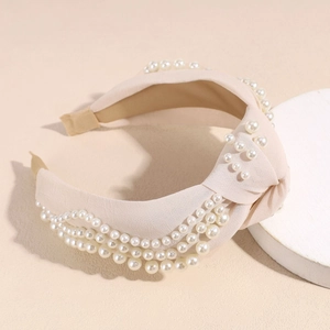 Détail d'un serre-tête noué en tissu crème orné d'élégantes perles blanches