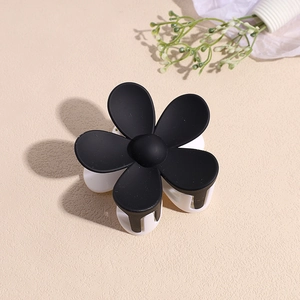 Gros plan sur une pince à cheveux fleur minimaliste avec une finition mate noire et blanche