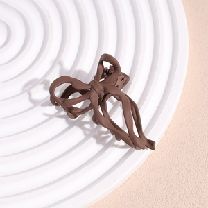 Detail shot of the matte dark coffee ribbon bow hair claw clip on a white plate