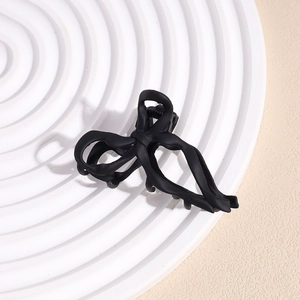 Detail view of the matte black bow hair claw clip on a minimalist textured plate