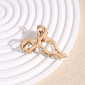 Detailed close-up of matte apricot bow hair claw clip on a textured decorative tray