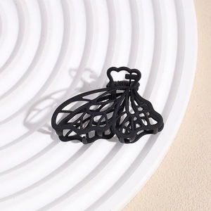 Detail of matte black hollow butterfly hair claw clip with metallic spring on a display tray
