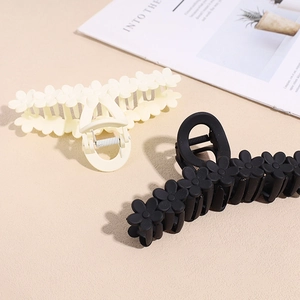 Detail of 13cm matte floral shark hair clips in beige and black colors shown on a magazine