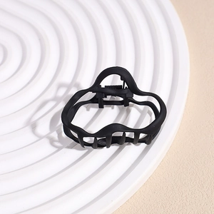 Detail of a matte black shark clip with irregular wave patterns on a white tray
