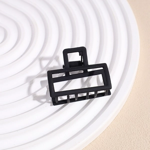 Detail view of small matte black rectangular claw clip on white textured background
