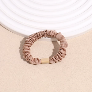 Detail of elegant satin scrunchie with beige resin accent in champagne gold color