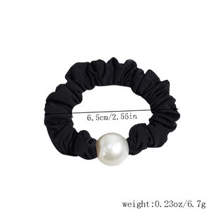 Detail view of a black satin scrunchie with a large pearl, showing 6.5cm diameter and weight