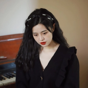 Dettaglio di cerchietto nero con perle indossato da modella vicino a un pianoforte