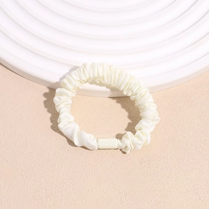 Close-up of cream pleated satin hair scrunchie with a matching rectangular buckle detail