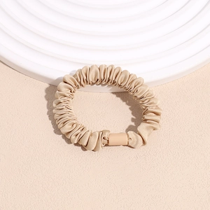 Detailed shot of pleated champagne satin scrunchie with soft silk texture and glossy finish